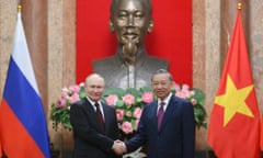 Vladimir Putin and To Lam shake hands between the Russian and Vietnamese flags and in front of a large bust of Ho Chi Minh