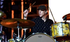 A man in a baseball cap plays the drums.