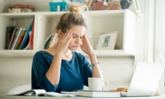 Portrait of an attractive woman at table hands at temples<br>Portrait of an attractive woman at table with cup and laptop, book, notebook on it, hands at her temples. Bookshelf at the background. Concept photo