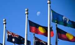 The moon behind the Australian flag, the Aboriginal flag and the Torres Strait Islands flag flying outside Parliament House in Canberra