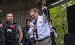 a man speaks into a microphone in front of armed militia members