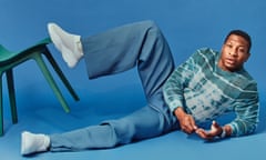 Jonathan Majors, lying on the floor with his foot up on a chair, wearing blue trousers and top by Amiri and shoes by Magnlens.