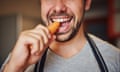 A man biting into a carrotman eating a carrot in his kitchen at home