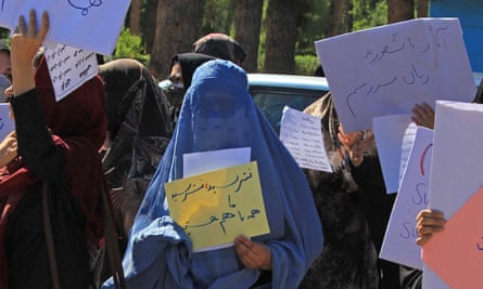 Afghan women in hijabs and burqas hold placards as they take part in a protest