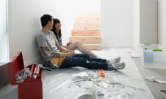 A couple, chatting and smiling, sitting on the floor of their home having a break from DIY