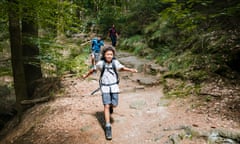 Young Boy Bounding Down Slop While Hiking With Family<br>A young boy wearing a rucksack bounding down a slope while out hiking a woodland trail with his family.