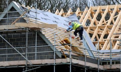 A construction worker on the roof of a partly built house surrounded by scaffolding