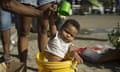 An infant is lifted out of a plastic bucket where it has been playing in a market in Brazil
