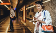 a young woman with a book checking her phone at a train station. 