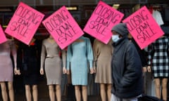 A pedestrian wearing a protective mask walks past mannequins and 'closing down sale' posters in a shop's window display