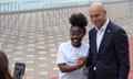 A teenaged African girl poses for a photo clasping hands with a bald European man in a dark suit