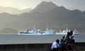 People sit on wall situated on the foreshore of the harbour in the Fiji capital of Suva