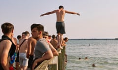 A young man walks along the railing ready to dive in to the estuary. Southend-on-Sea. 2022.