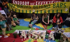 Mothers and their small children sitting on the floor with campaign banners behind them and the name Aisha spelled out in flowers in front of them