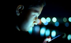 Young white boy looking at cellphone in darkness.