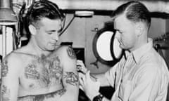 John Paterson of Ballarat, Victoria, displays tattoos from every port he has visited, as surgeon lieutenant Vic Hercus of Sydney gives him an inoculation