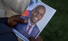 Black hand holds photo of black man in blue suit and striped red and blue tie.