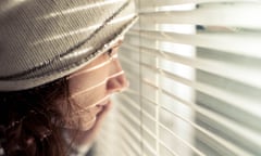 Girl with long dark-reddish hair wearing pale woollen hat looking through window blinds
