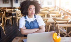 Sad woman sitting in cafeteria and using laptop<br>Sad woman sitting arms crossed in cafeteria and looking at laptop.