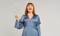 Lorraine Kelly standing holding a flower with her head back laughing, wearing a blue wrap dress and gold heels