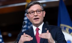 Middle-aged white man with tortoiseshell glasses and gray coiffed hair and red tie speakers and gestures with both hands held before him.