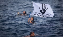 Volunteers from the " "Flotilla Watermelon", part of a larger concentration of boats protesting against oil exploration in Spain's Canary Islands by national outfit REPSOL, hold up flags as they swim between the island of Lanzarote and Fuerteventura during their demonstration off the archipelago.