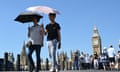 People walking near the Houses of Parliament use umbrellas to protect themselves from the sun