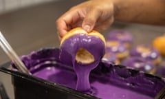 A doughnut being dipped in purple icing