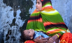 A Rohingya refugee woman looks on as she holds her child at a temporary camp