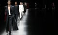 Models walk the runway at the Gucci collection show during Milan fashion week menswear wearing black and white tailored trousers and jackets and coats.
