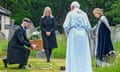 A person kneels to place a small coffin on the ground before its burial