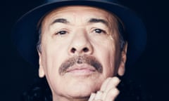 Carlos Santana in a trilby and with his hands together in front of him