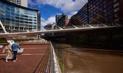 Bridge over river in urban area with couple walking along bank