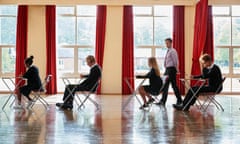 Teacher supervises teenage students in uniform sitting examination in school hall