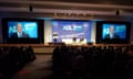 Three people stand on stage and speak during an ADL summit, while a large crowd watches