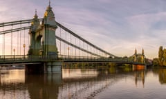 Hammersmith Bridge v<br>Hammersmith Bridge, London, UK. September 15, 2018. Scene shows the Hammersmith Bridge spanning across the River Thames. The street lights are illuminating a light orange glow in the dawn light.