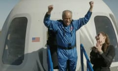 Man wearing blue jumpsuit with hands up in air in front of white structure