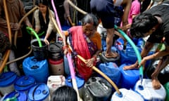 People direct hoses from a water truck into the holes of large plastic barrels