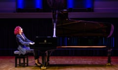 Concert pianist Joanna MacGregor, in a silk suit and high heels and with curly shoulder-length hair, closes her eyes as she plays a grand piano on a wooden floor