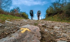 Two pilgrims follow a yellow waymark on the Camino de Santiago.