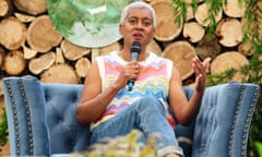 Arit Anderson sitting on a small sofa, talking into a microphone, against a backdrop of cut logs and branches