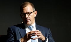 Daniel Křetínský speaks at a conference in Prague, October 2023: he is in his late 40s with short-cropped fairish hair and glasses, and is seen against a black backdrop wearing a dark blue suit, white shirt and pale blue tie; his hands are held up in front of his body with fingers pushed together as he speaks