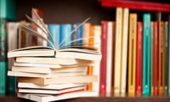 Stack of books on a wooden library shelf, one of them open on top, multicoloured book spines background