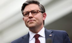 man with reddish glasses and gray hair wears a suit with a red tie