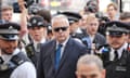 Huw Edwards, wearing a dark blue suit and black sunglasses, surrounded by police and members of the media outside court