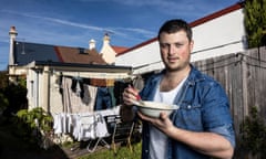 A man in his 30s in a denim button shirt stands heroically in front of a washing line, holding a white bowl of porridge.