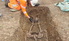 Archaeologist brushing decapitated skeleton lying in shallow grave.