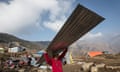 A woman carries a metal roof panel to rebuild her damaged house in Laprak, in Nepal’s Gorkha district.