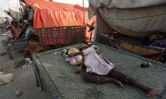 child rests on makeshift bed among shelters