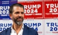 Donald Trump Jr in front of a wall plastered with Trump 2024 posters.